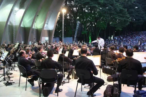 Músicos se apresentando para plateia em concha acustica